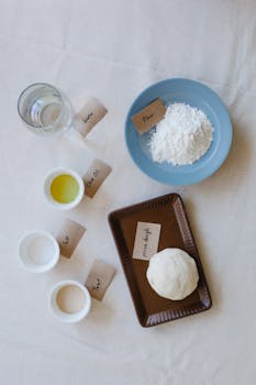 Overhead view of pizza dough ingredients including flour, oil, and water on a table.