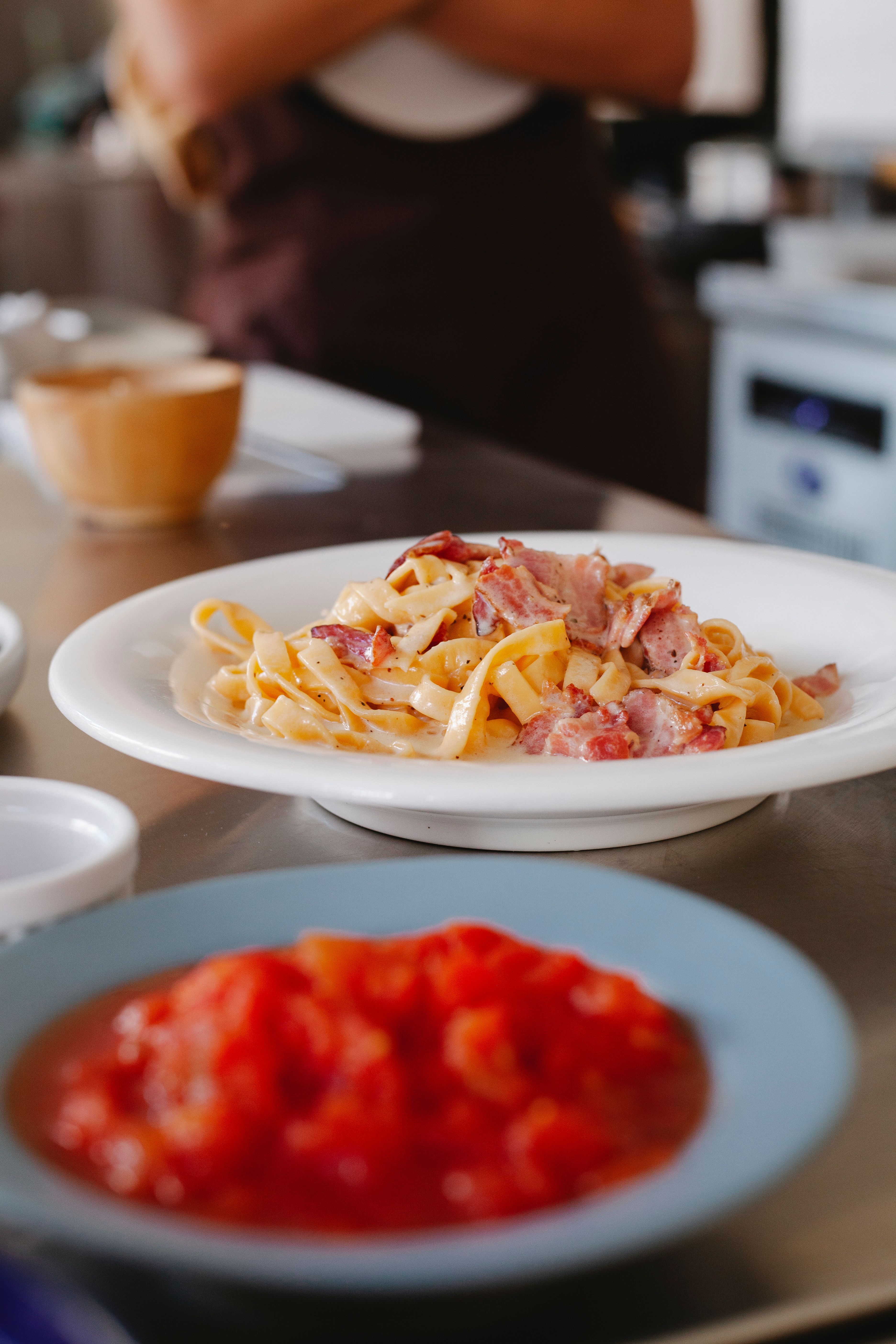 Tantalizing pasta with bacon served on a white plate in a cozy kitchen setting.
