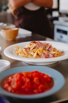 Tantalizing pasta with bacon served on a white plate in a cozy kitchen setting.