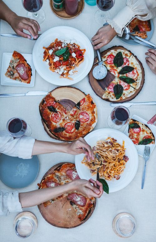 Free Top view of hands sharing Italian dishes like pizza and pasta at a social gathering. Stock Photo