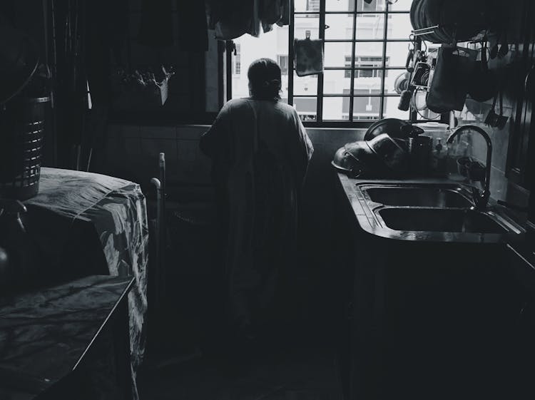 Woman Looking Out A Kitchen Window In An Apartment In City