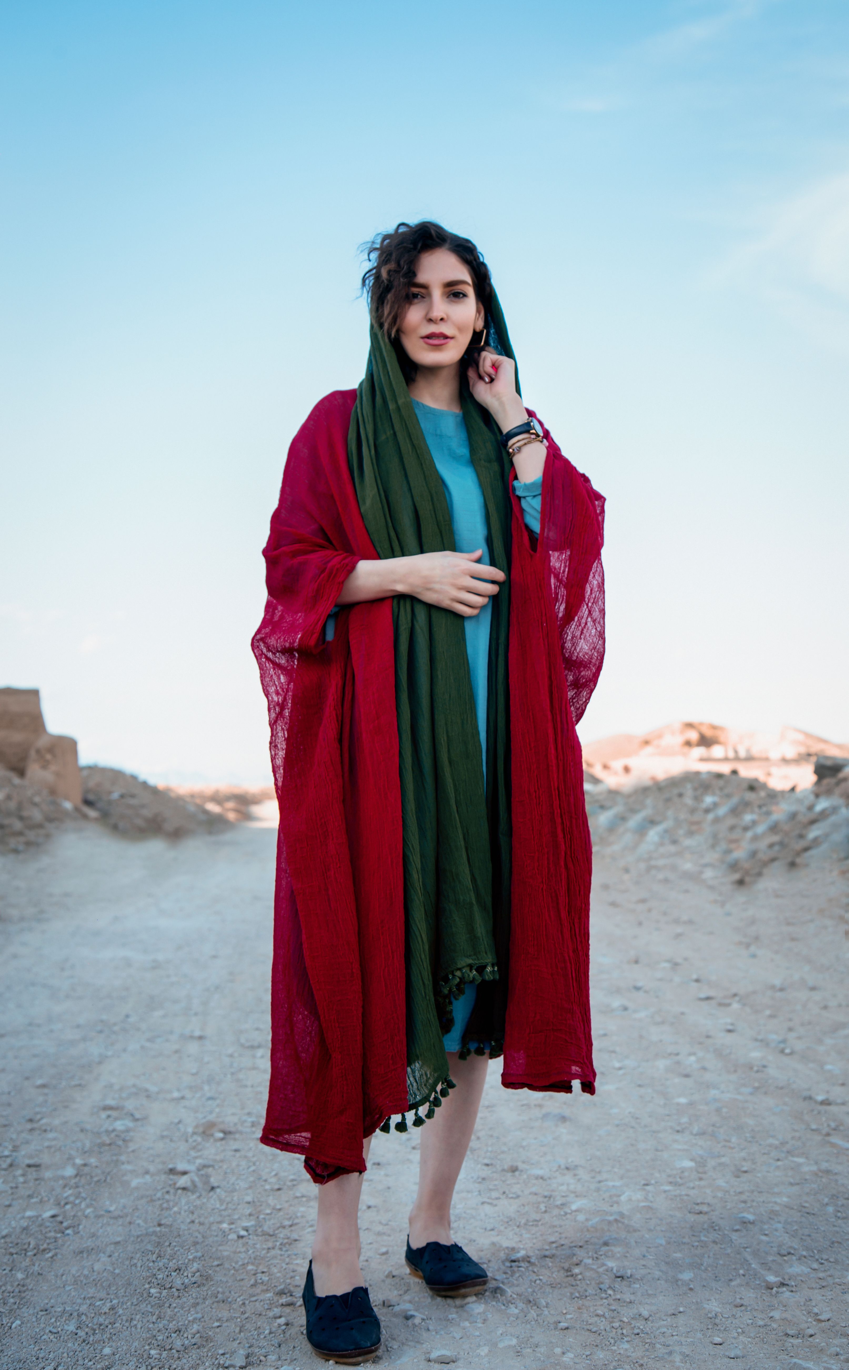 Stylish woman in vibrant attire standing on a sandy road under a blue sky.