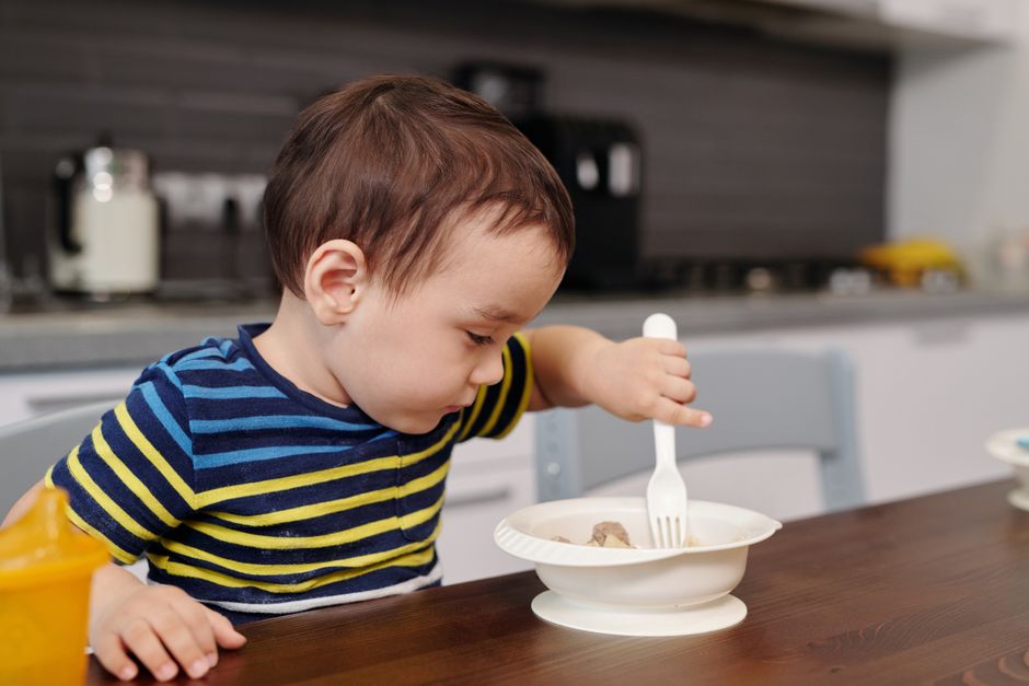 Menino comendo com garfo na mesa da cozinha