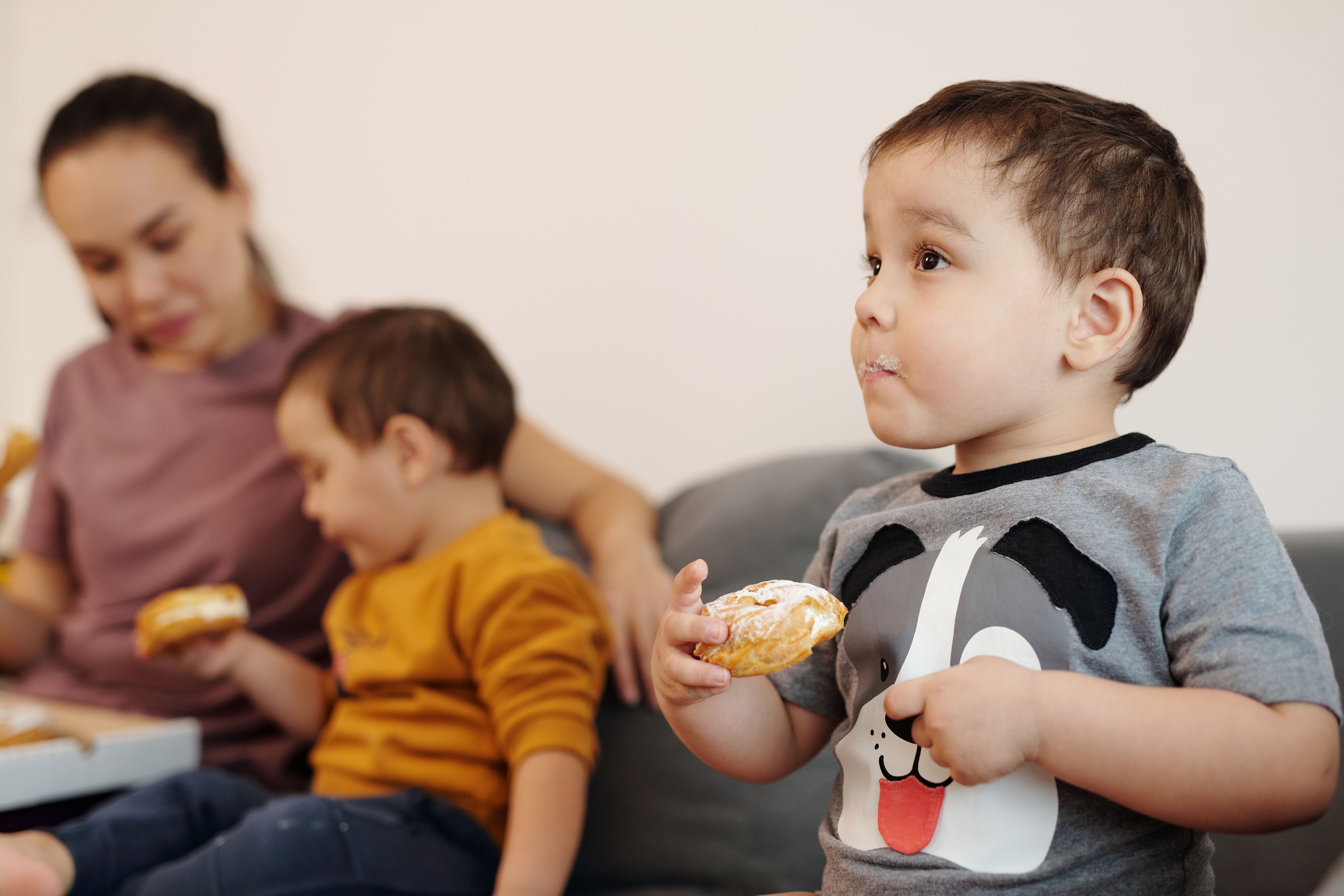 A mother sitting with her two young sons enjoying donuts together indoors.