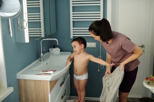 A mother helps her young son at the sink, creating a warm parenting moment.