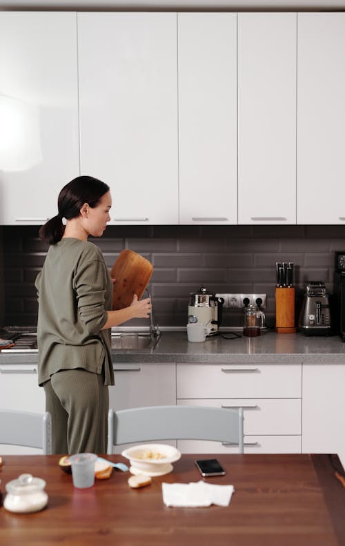 Free A Woman Holding a Wooden Chopping Board while Standing in the Kitchen Stock Photo
