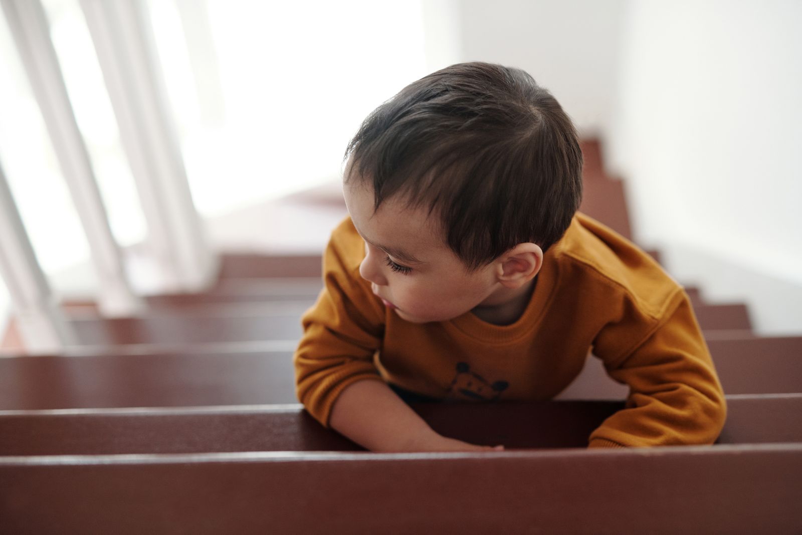 Young child sitting on wooden stairs inside a home near the bottom landing