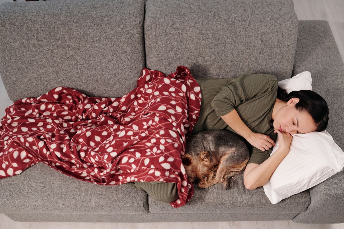 Mulher dormindo no sofá acompanhada de seu cachorro