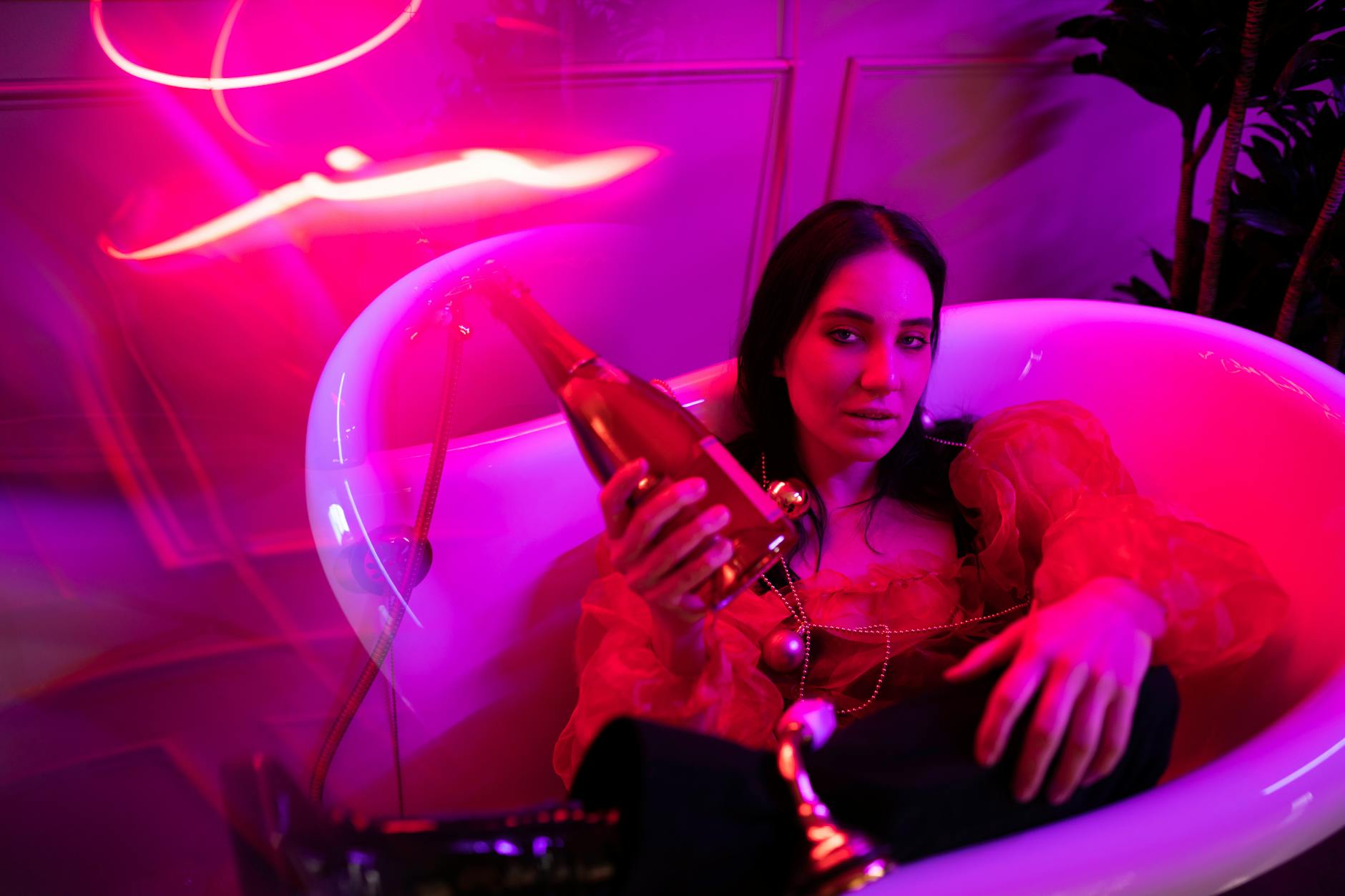 A woman in a red blouse holding champagne, surrounded by neon lights.