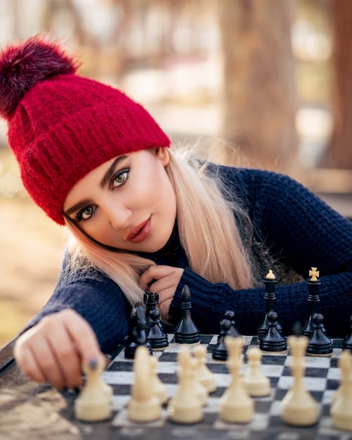 Photo of a Woman in a Blue Sweater Posing Near a Chess Board