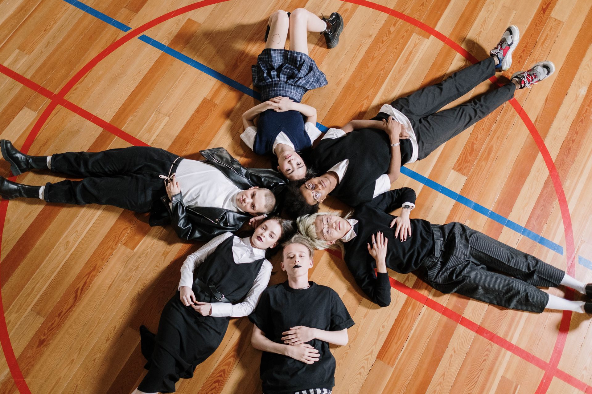 A diverse group of young adults lying on a gym floor forming a star shape.