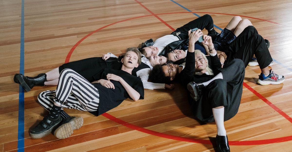 A group of diverse friends lying on a gym floor, capturing a selfie together, unified in a sports hall.