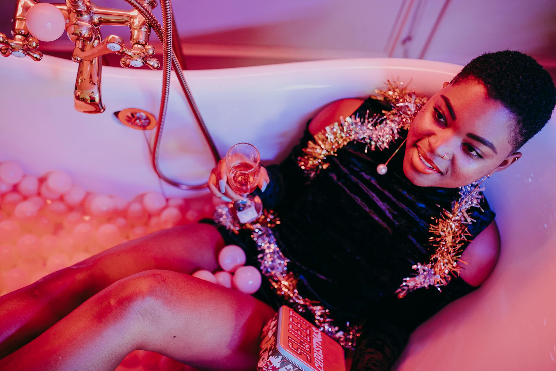 A joyful woman enjoys a festive moment in a bathtub with champagne and decorations.