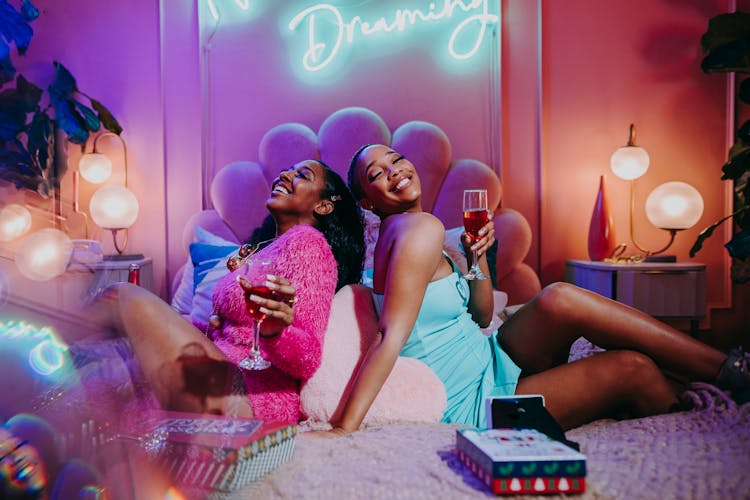 Women Sitting On Bed Holding Champagne Glasses