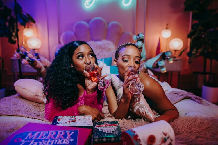 A Two Women Drinking On The Bed Together 