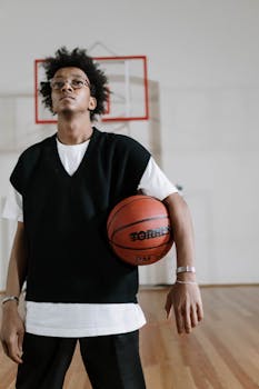 Confident young man holding a basketball in an indoor gym setting. Athletic and stylish.