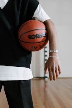 Close-up of a basketball player holding a ball indoors on hardwood floor.
