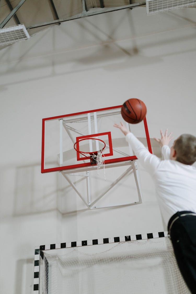 Low Angle Shot Of A Man Throwing A Ball Into A Basket At A School Gym 