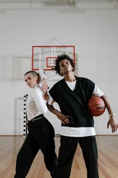 Two stylish adults pose confidently in a basketball gym, exuding sport and fashion vibes.