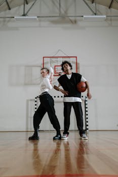 Two teenagers posing with basketball on an indoor court, embracing active lifestyle.