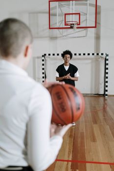 Two men engaged in basketball practice indoors, one holding a ball.