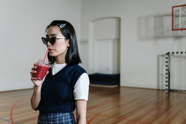 Girl Wearing Sunglasses And Drinking Juice In A School Gym 