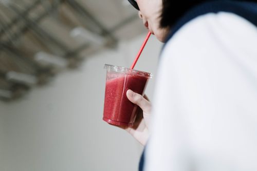Free Close up of a woman holding and drinking a strawberry smoothie through a red straw. Stock Photo