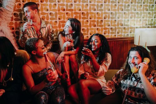 Free Group of diverse young adults enjoying a lively indoor celebration with drinks and laughter. Stock Photo