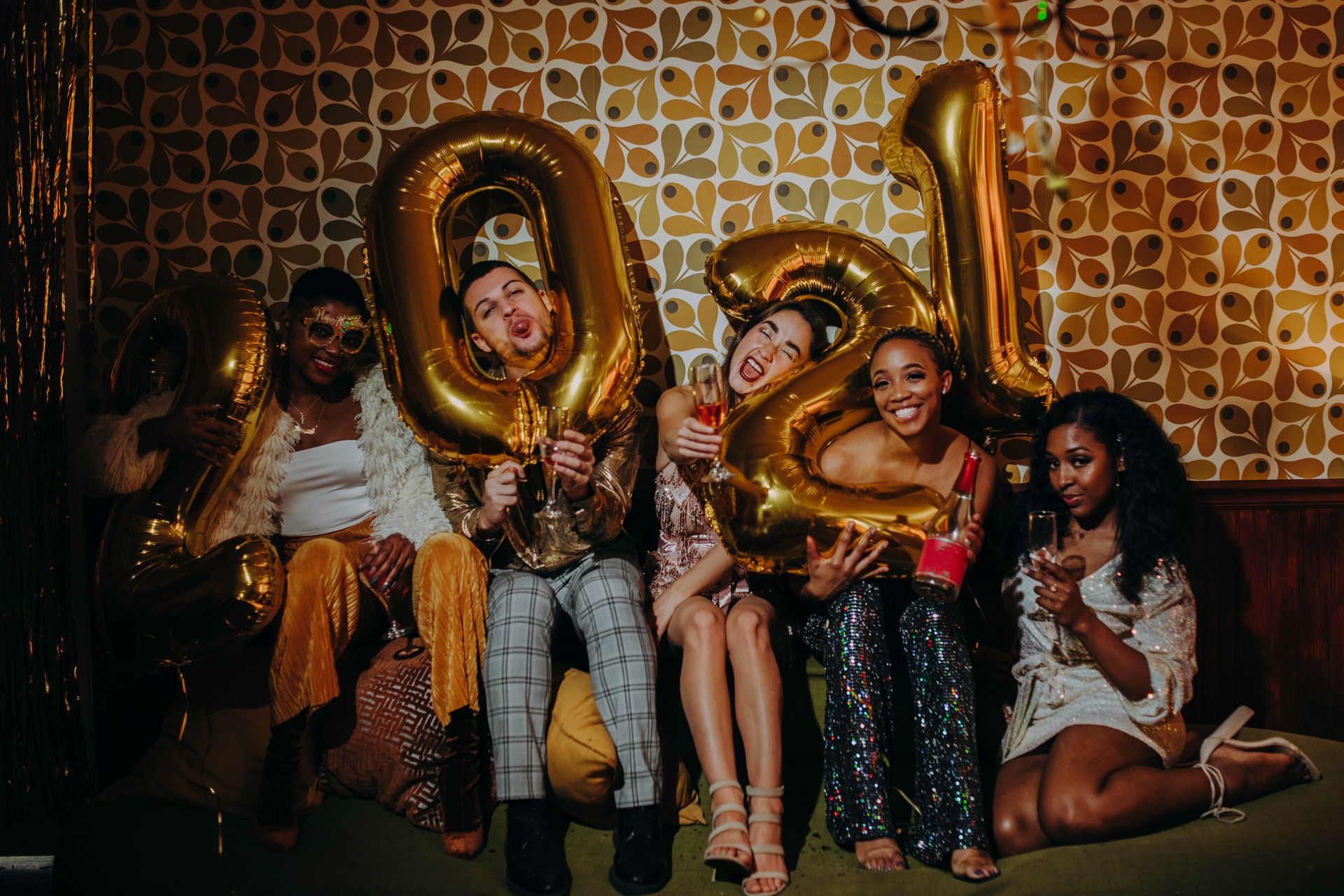 Diverse group celebrating New Year's Eve with balloons and champagne indoors.