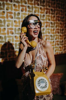 A joyful woman with New Year's glasses and vintage rotary phone in a festive setting.