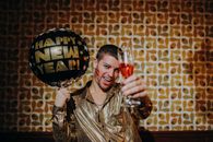 Man celebrating New Year's Eve with a balloon and champagne, capturing festive vibes indoors.