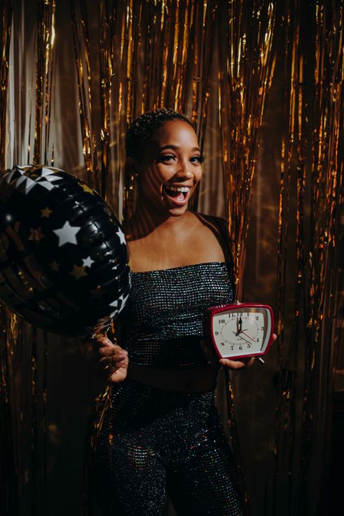 Free Happy woman holding a balloon and clock, celebrating New Year's Eve indoors with festive decor. Stock Photo