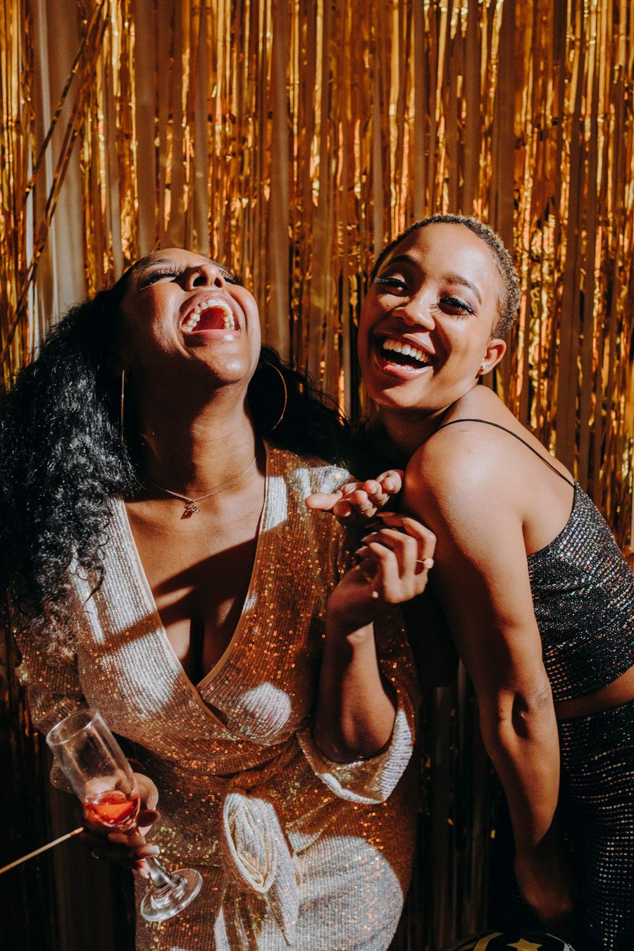 Two friends laughing at a party in front of a golden backdrop