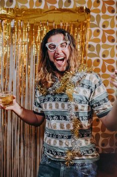 Joyful adult celebrating with a drink and wearing festive accessories at a retro-themed party.