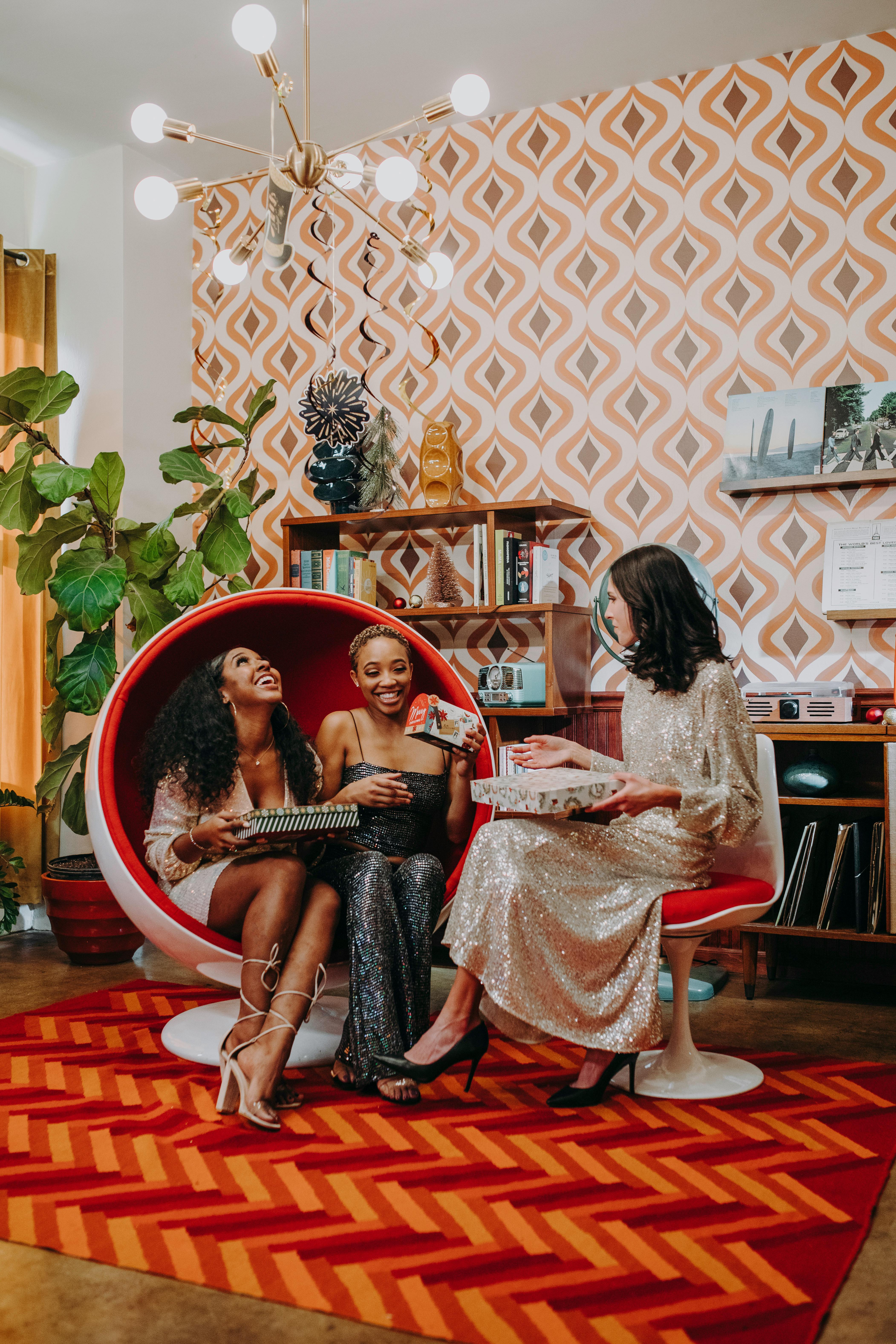 Three women in a retro living room exchanging gifts and enjoying the festive atmosphere.