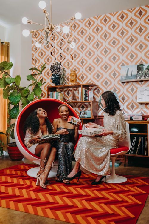Free Three women in a retro living room exchanging gifts and enjoying the festive atmosphere. Stock Photo