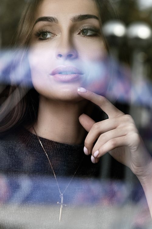 Free Through glass crop young pretty female touching chin tenderly and looking away dreamily Stock Photo