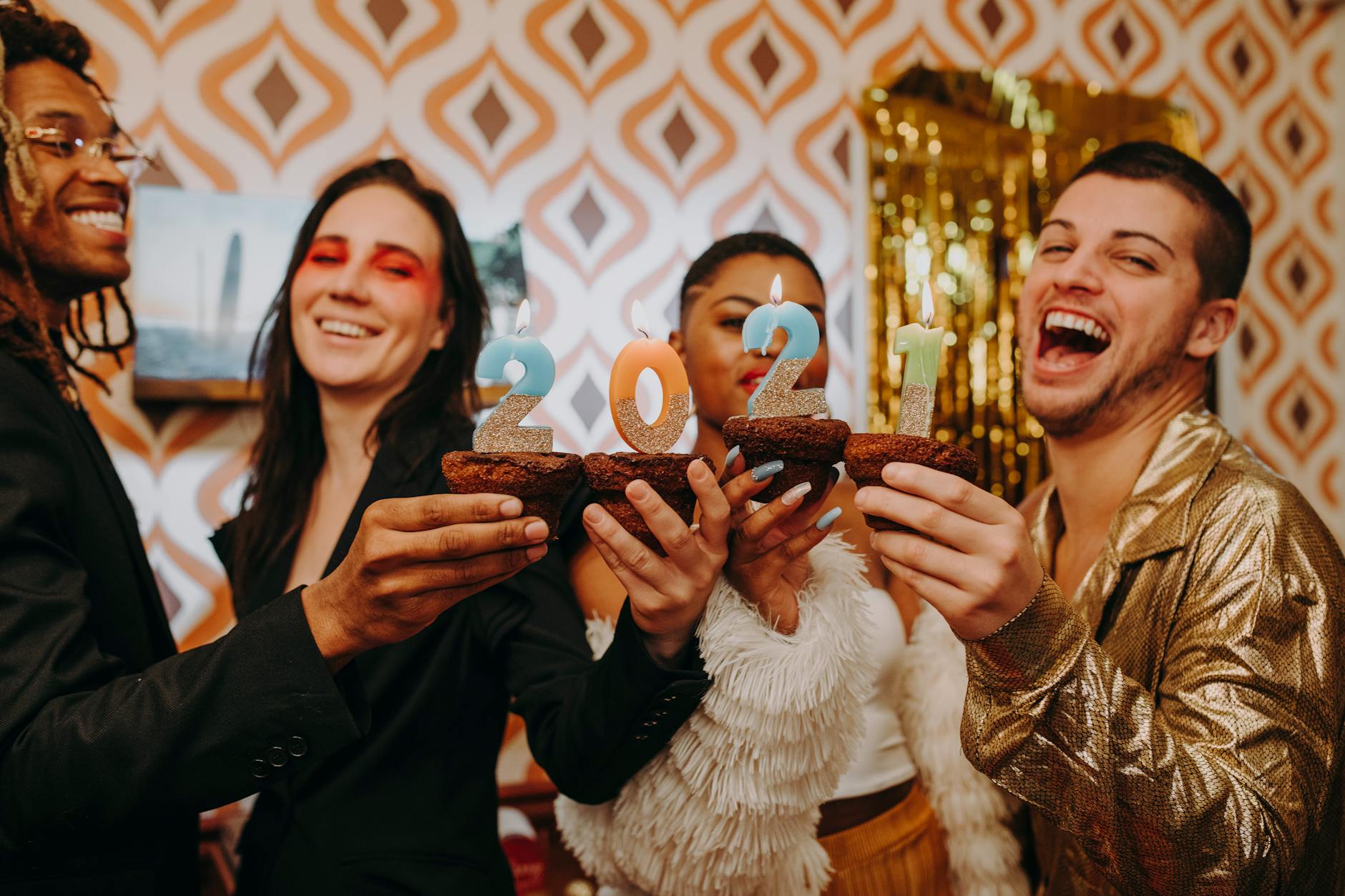 A diverse group of friends celebrate New Year's Eve with 2021 candles indoors.