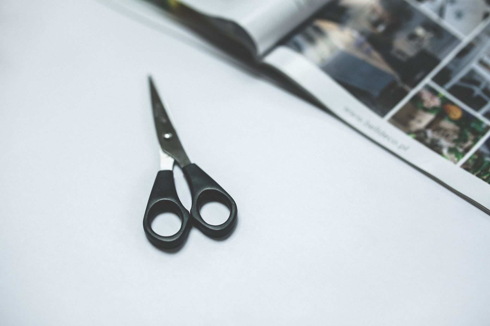 Black-handled scissors resting on a white surface next to an open magazine.