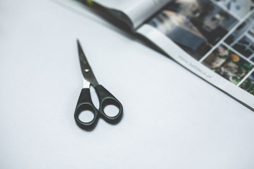 Black-handled scissors resting on a white surface next to an open magazine.