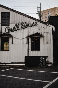 Cozy grill house exterior in Narita, Japan, featuring a vintage neon sign and corrugated metal facade.