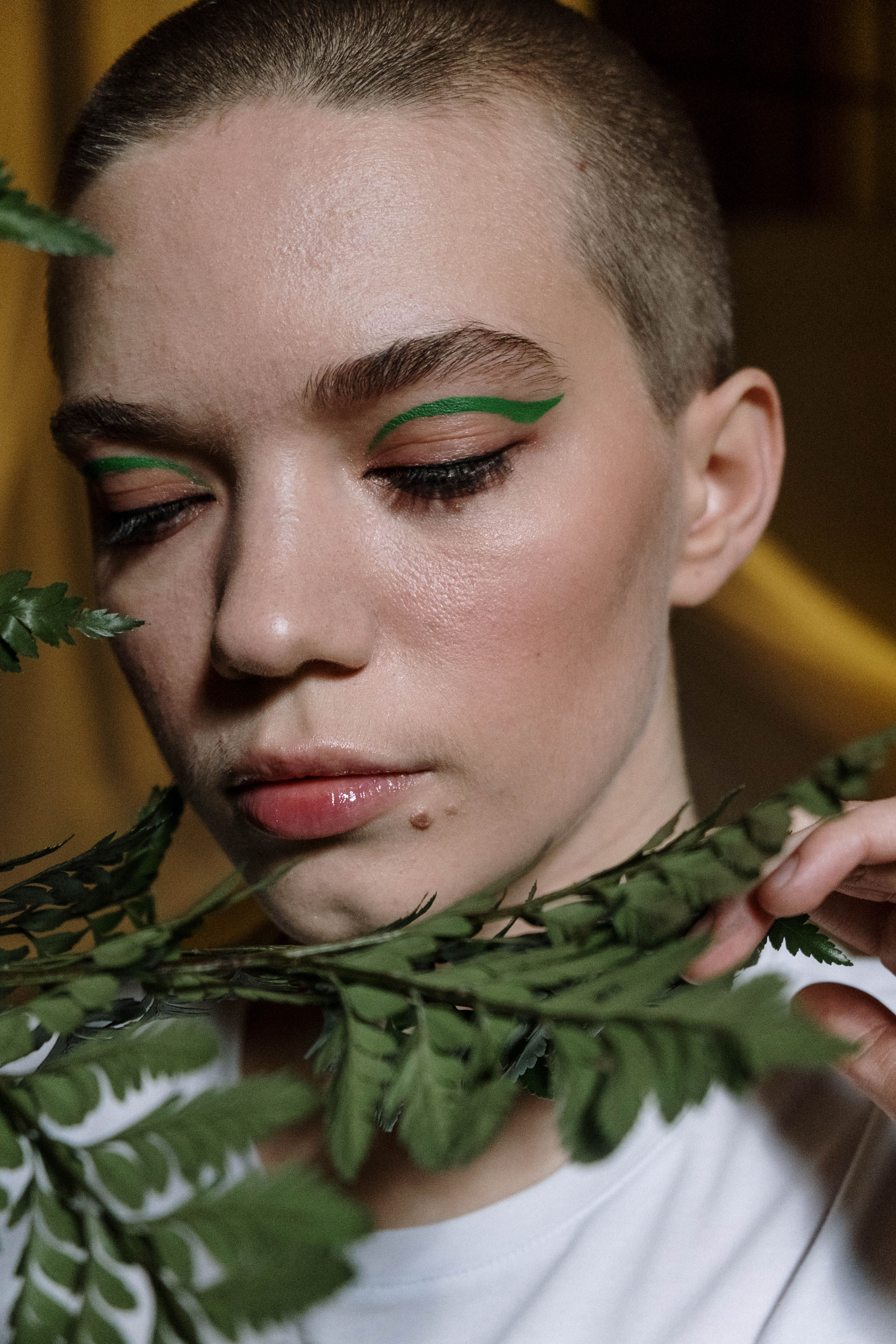 Close-up portrait of a woman with green eye makeup and fern leaves.