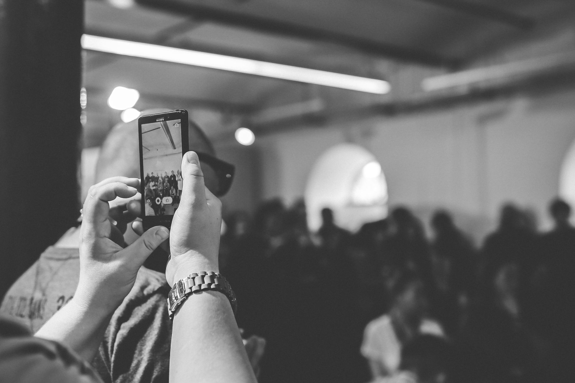 Black and white photo of a person using a smartphone to take photos at an event.