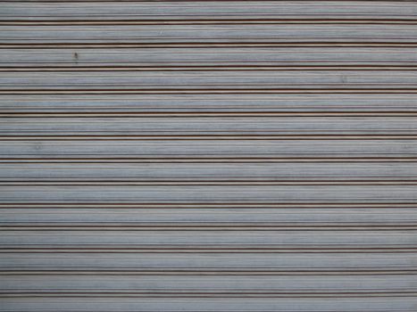 Close-up of a gray metal shutter with repeated horizontal lines, creating a striped pattern.