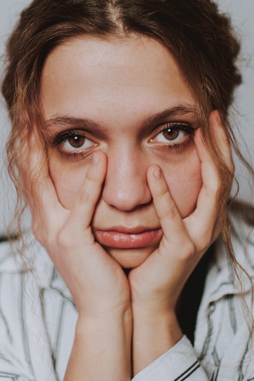 Crop anxious female covering face with hands while standing in room and looking at camera