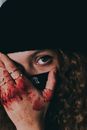 Unrecognizable female in black mask and hat covering face with hand in blood and looking at camera