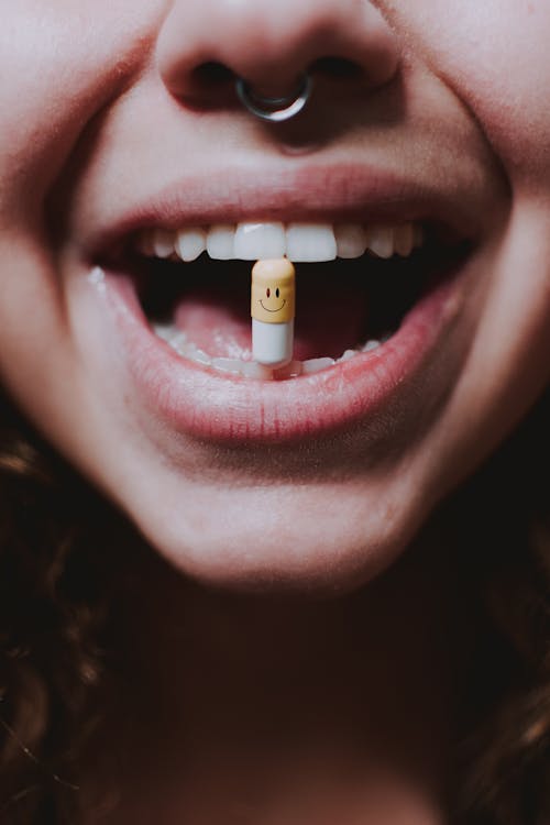 Free Faceless woman with pill in teeth and nose piercing Stock Photo