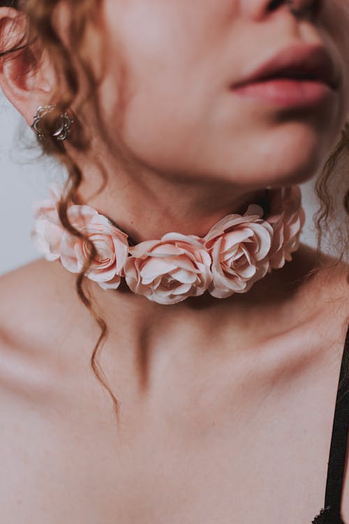 Crop anonymous female in pink flowers on choker with earring on white background in light place