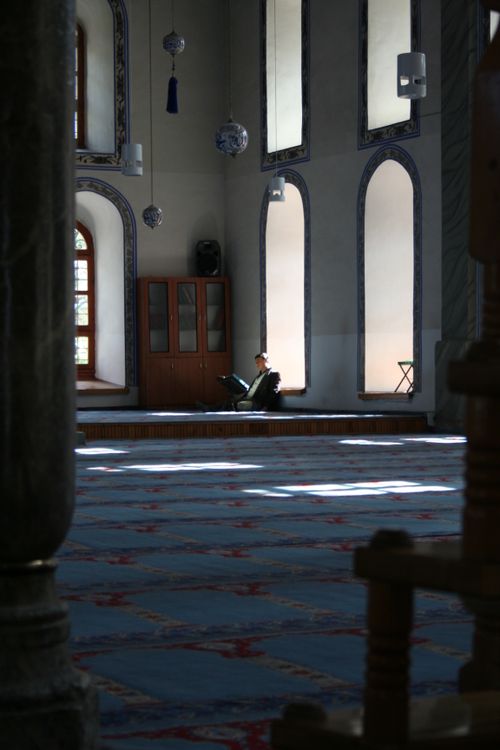 Free A man sitting alone in a sunlit mosque interior reading. Peaceful and contemplative. Stock Photo