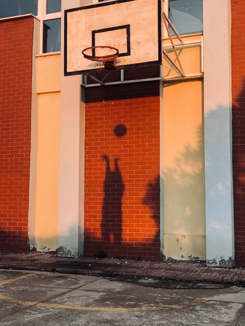 Shadow of a basketball player shooting on a brick wall during sunset.